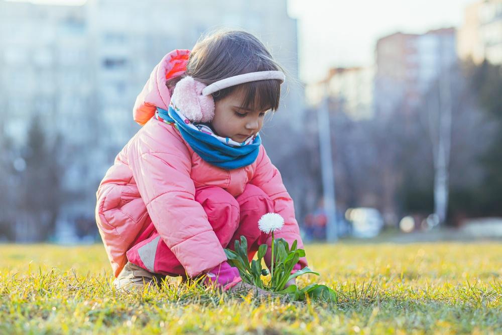 ילדה בגינה כורעת לראות ולהריח פרח